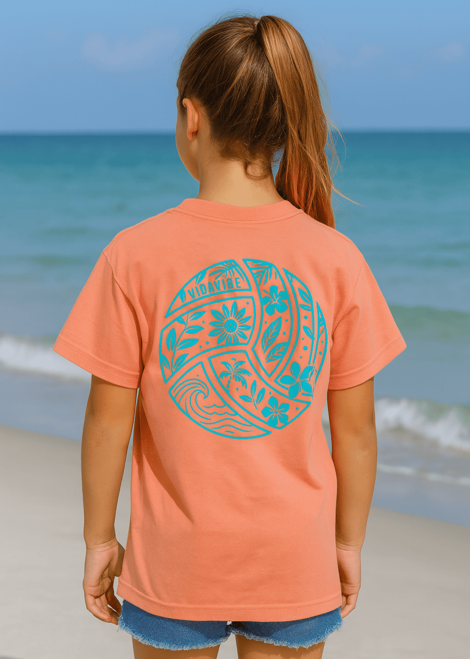 Girl wearing a coral t-shirt with a blue graphic design on the beach